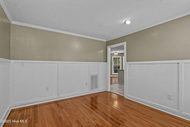 empty room featuring visible vents, ornamental molding, wainscoting, wood finished floors, and a textured ceiling