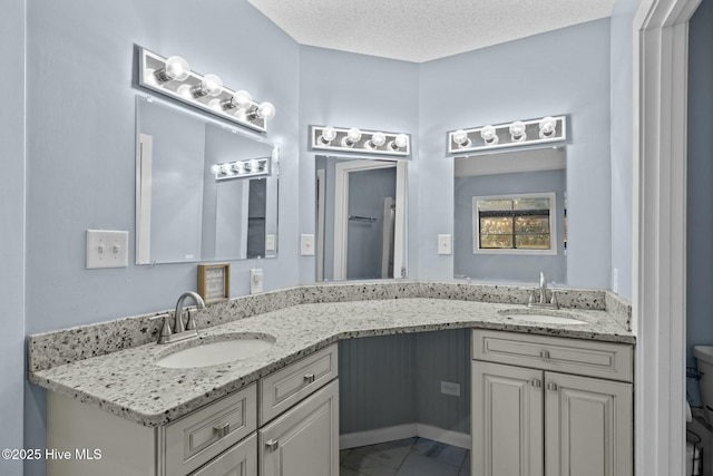 full bath with a sink, a textured ceiling, double vanity, and toilet