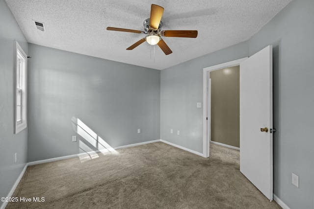 spare room featuring visible vents, carpet floors, a textured ceiling, and a ceiling fan