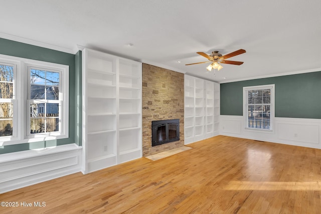 unfurnished living room featuring built in shelves, wood finished floors, ceiling fan, and ornamental molding