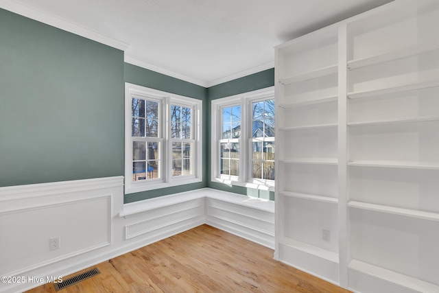 interior space featuring visible vents, light wood-style flooring, wainscoting, and ornamental molding