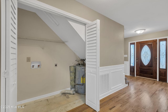 foyer with a wainscoted wall, visible vents, light wood finished floors, electric water heater, and a decorative wall