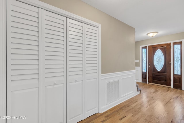 foyer entrance with light wood-type flooring, visible vents, and wainscoting