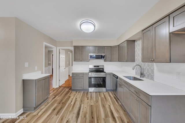 kitchen featuring light wood finished floors, gray cabinets, a sink, decorative backsplash, and appliances with stainless steel finishes