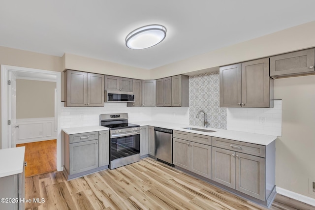 kitchen with a sink, gray cabinets, light wood finished floors, and stainless steel appliances