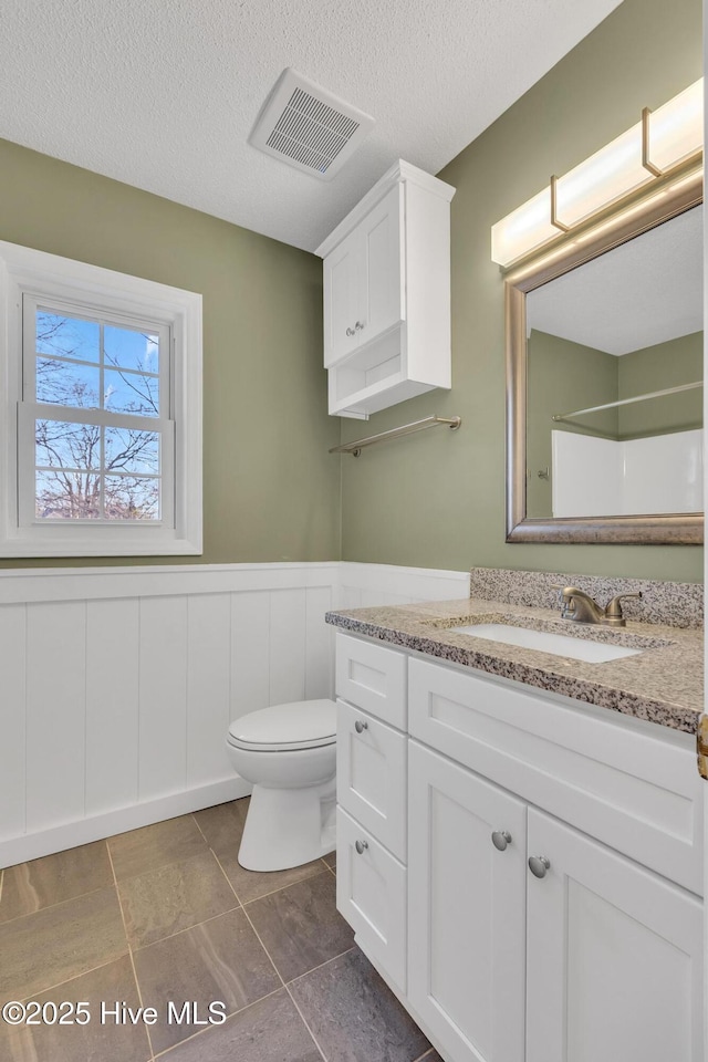 full bath featuring a wainscoted wall, toilet, visible vents, and a textured ceiling