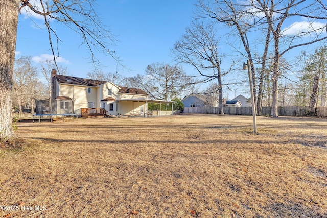 view of yard with a carport, a trampoline, and fence