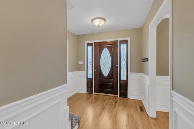 entrance foyer with a wainscoted wall, visible vents, light wood-style flooring, and a decorative wall