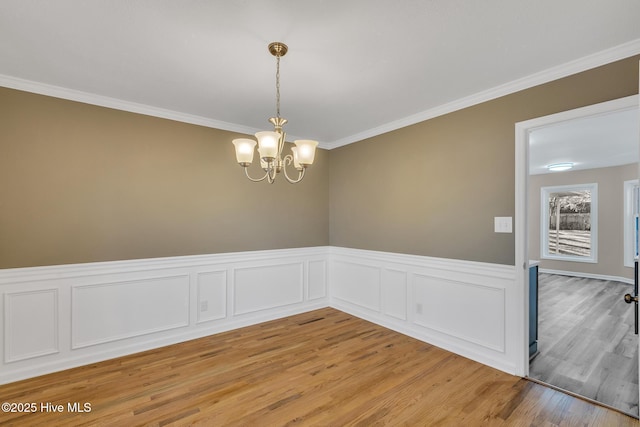 spare room featuring a wainscoted wall, a notable chandelier, light wood-type flooring, and ornamental molding