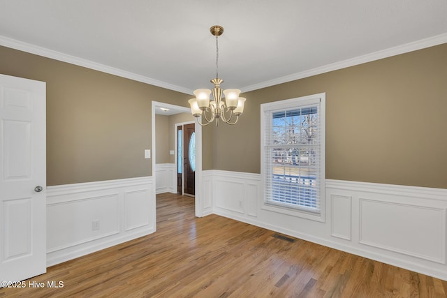 unfurnished dining area featuring light wood-style floors, a notable chandelier, visible vents, and wainscoting