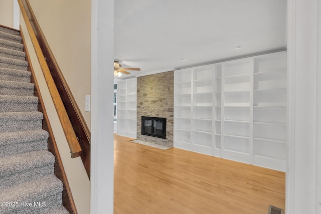 stairway featuring visible vents, built in features, wood finished floors, a fireplace, and ceiling fan