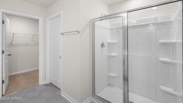 bathroom featuring a walk in closet, baseboards, and a stall shower