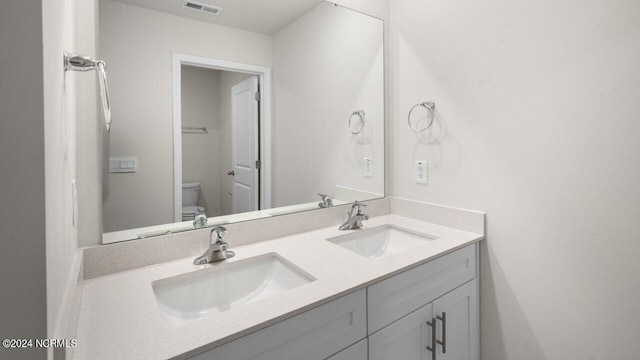 bathroom featuring double vanity, toilet, visible vents, and a sink