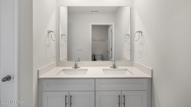 bathroom featuring a sink, visible vents, toilet, and double vanity