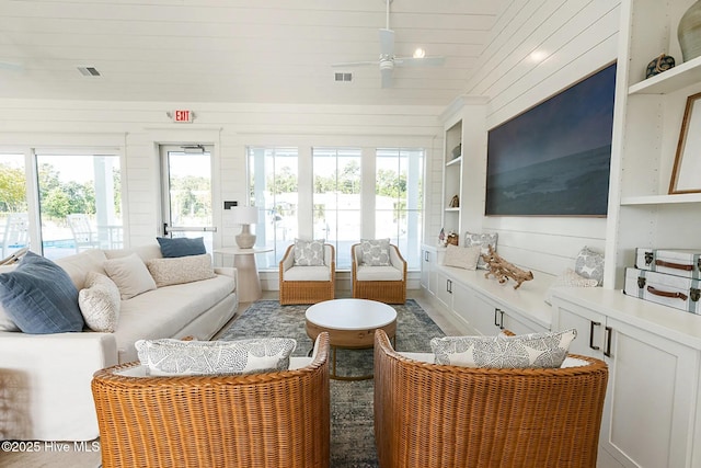 living area with built in features, visible vents, wooden walls, and a ceiling fan