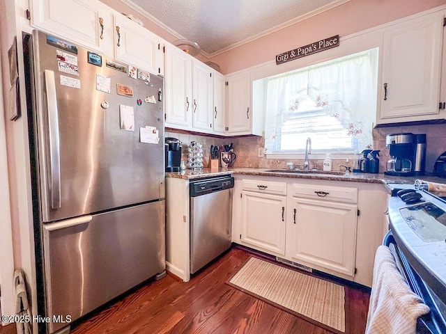 kitchen with dark wood-type flooring, ornamental molding, a sink, appliances with stainless steel finishes, and white cabinets