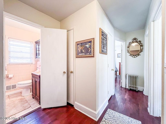 corridor with visible vents, dark wood-style floors, radiator, tile walls, and baseboards