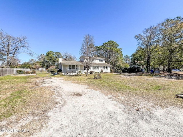 view of front of home featuring a front lawn, fence, driveway, and a chimney