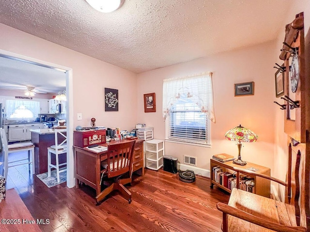 home office featuring visible vents, a ceiling fan, a textured ceiling, dark wood-style floors, and baseboards