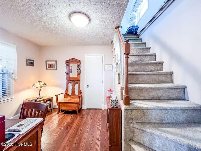 stairs with wood finished floors, baseboards, and a textured ceiling