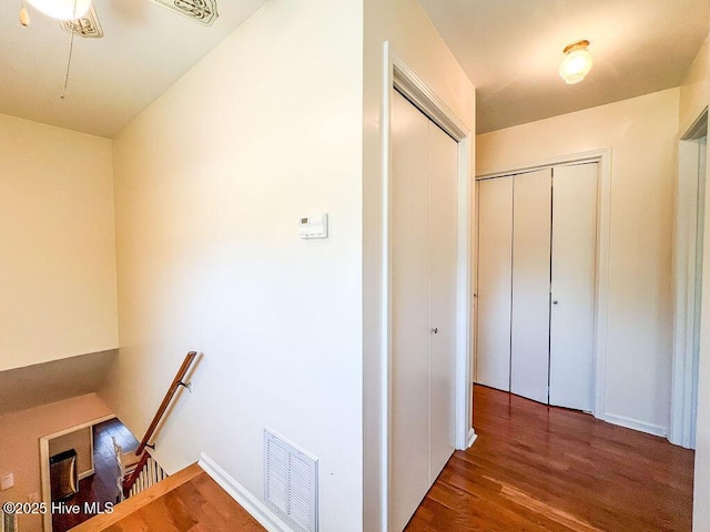 corridor with wood finished floors, an upstairs landing, visible vents, and baseboards