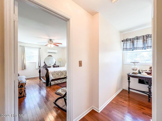 hall featuring an AC wall unit, baseboards, and hardwood / wood-style flooring