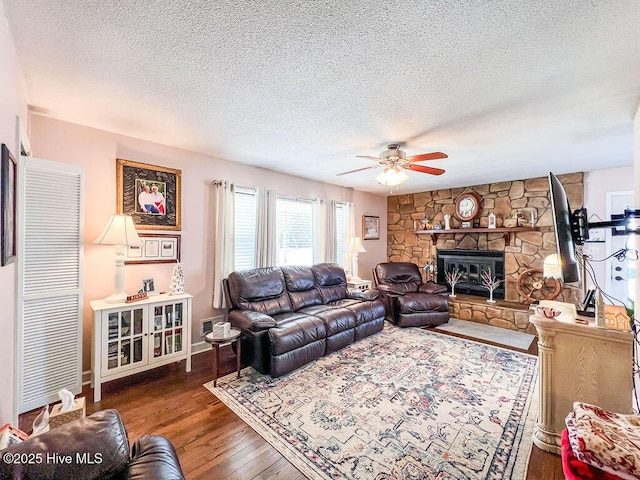 living area featuring a stone fireplace, a textured ceiling, wood finished floors, and ceiling fan