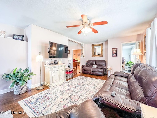 living area featuring a textured ceiling, wood finished floors, baseboards, and ceiling fan