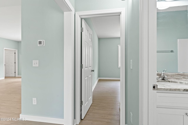 corridor with baseboards, light wood finished floors, and a sink