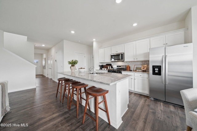 kitchen with an island with sink, a sink, appliances with stainless steel finishes, white cabinets, and dark wood-style flooring