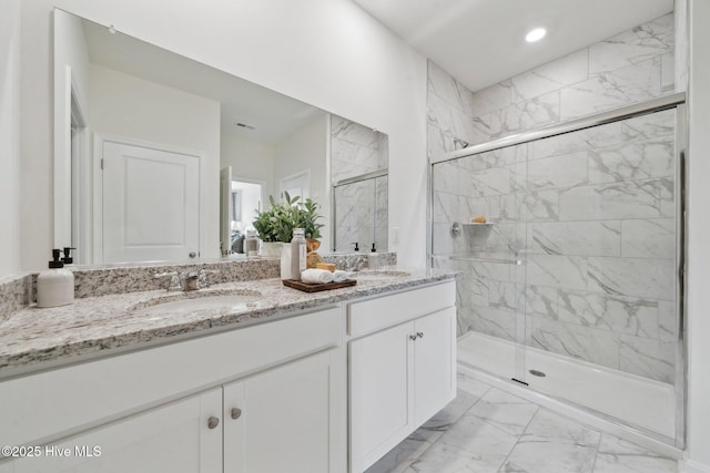 full bath with double vanity, marble finish floor, a marble finish shower, and a sink