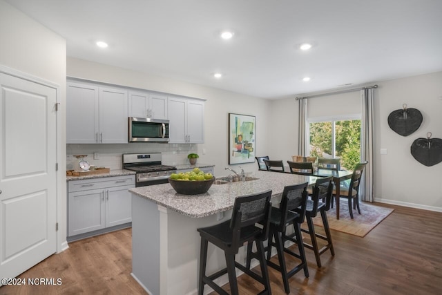 kitchen featuring tasteful backsplash, appliances with stainless steel finishes, light stone counters, and dark wood-style flooring