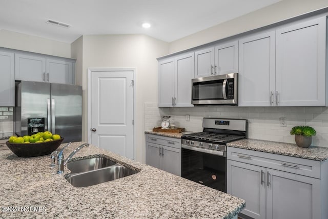 kitchen featuring visible vents, light stone countertops, decorative backsplash, stainless steel appliances, and a sink