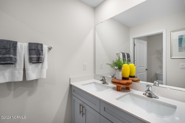 bathroom with a sink, toilet, and double vanity