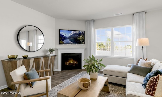 living room with wood finished floors, visible vents, a warm lit fireplace, and baseboards