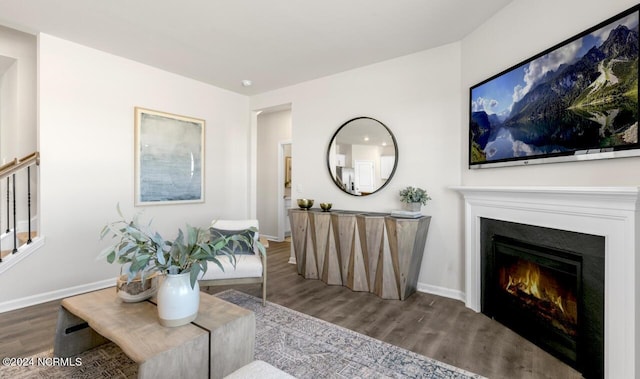 living area featuring stairway, baseboards, a lit fireplace, and wood finished floors