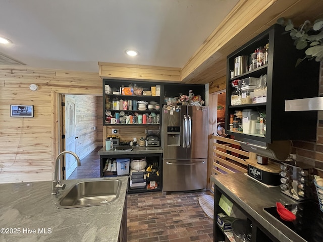 kitchen featuring open shelves, brick floor, a sink, stainless steel refrigerator with ice dispenser, and wood walls