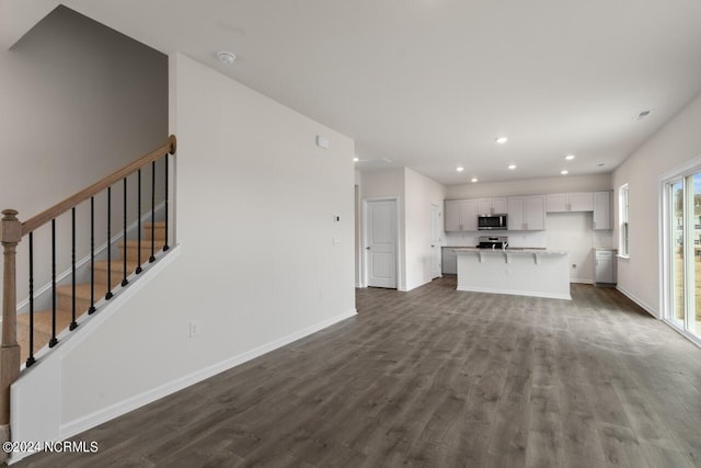 unfurnished living room featuring recessed lighting, baseboards, stairs, and dark wood-style flooring