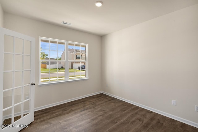 empty room with dark wood finished floors, visible vents, and baseboards