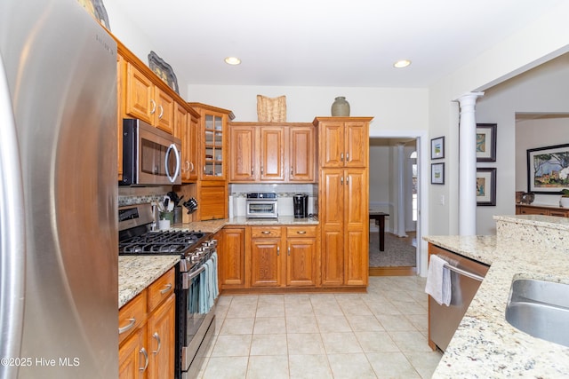 kitchen with light stone counters, stainless steel appliances, glass insert cabinets, brown cabinets, and backsplash