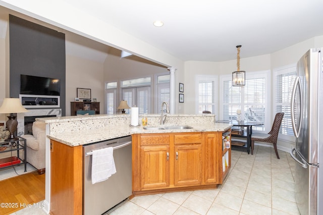 kitchen featuring light stone countertops, open floor plan, plenty of natural light, stainless steel appliances, and a sink