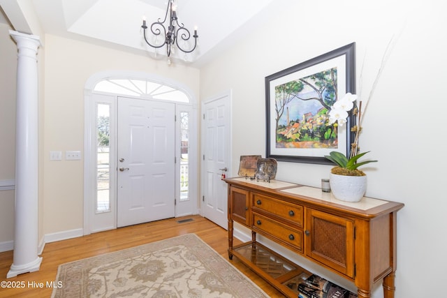 entryway with light wood finished floors, baseboards, a tray ceiling, a notable chandelier, and ornate columns