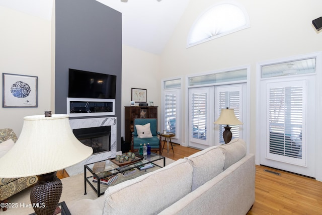 living room with a high end fireplace, visible vents, a wealth of natural light, and wood finished floors