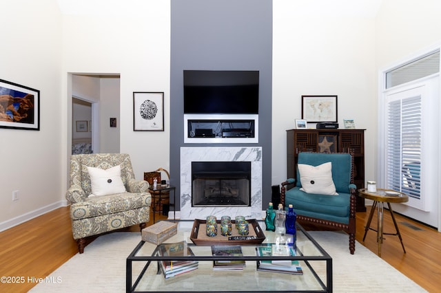 living room featuring a high end fireplace, visible vents, a towering ceiling, and wood finished floors