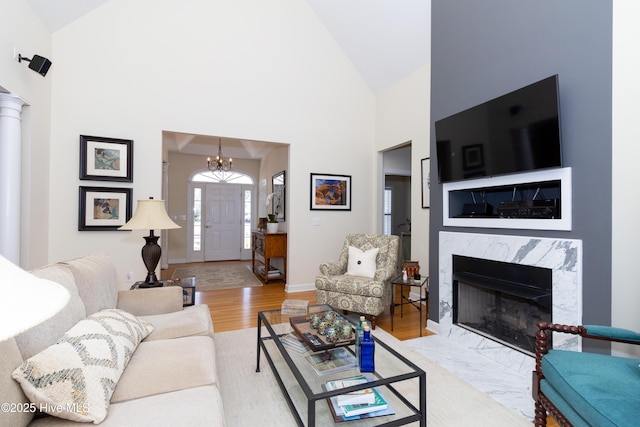 living area featuring high vaulted ceiling, wood finished floors, an inviting chandelier, a premium fireplace, and baseboards