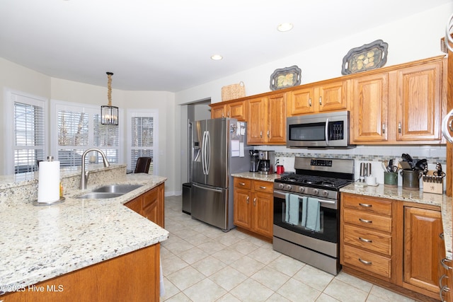 kitchen with a sink, backsplash, stainless steel appliances, brown cabinetry, and light stone countertops