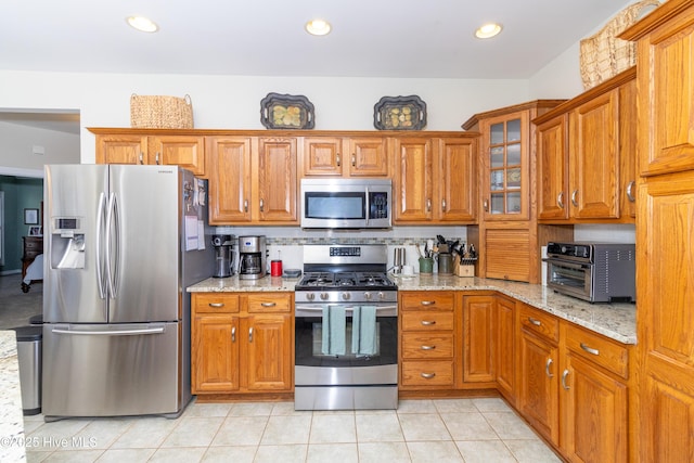 kitchen with brown cabinets, stainless steel appliances, and light stone countertops