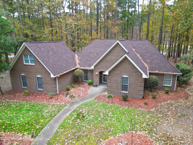 view of front of house with brick siding, a wooded view, a front lawn, and a shingled roof