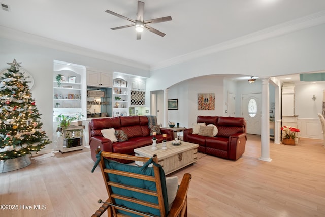 living area featuring ornamental molding, ornate columns, light wood-style floors, arched walkways, and a ceiling fan