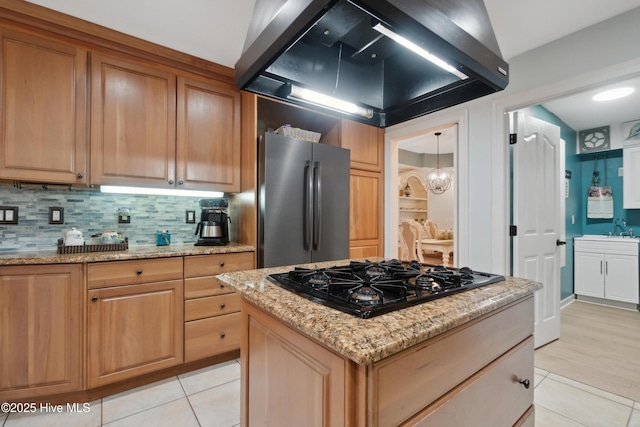 kitchen featuring black gas cooktop, decorative backsplash, light stone countertops, and freestanding refrigerator